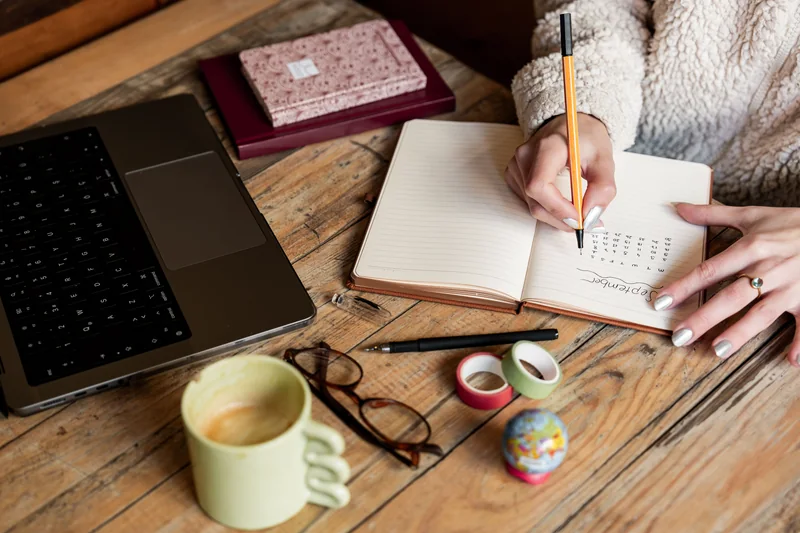Hands creating a monthly study plan in a notebook